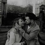 A romantic couple shares a tender moment on a bench in Bath, UK city street.