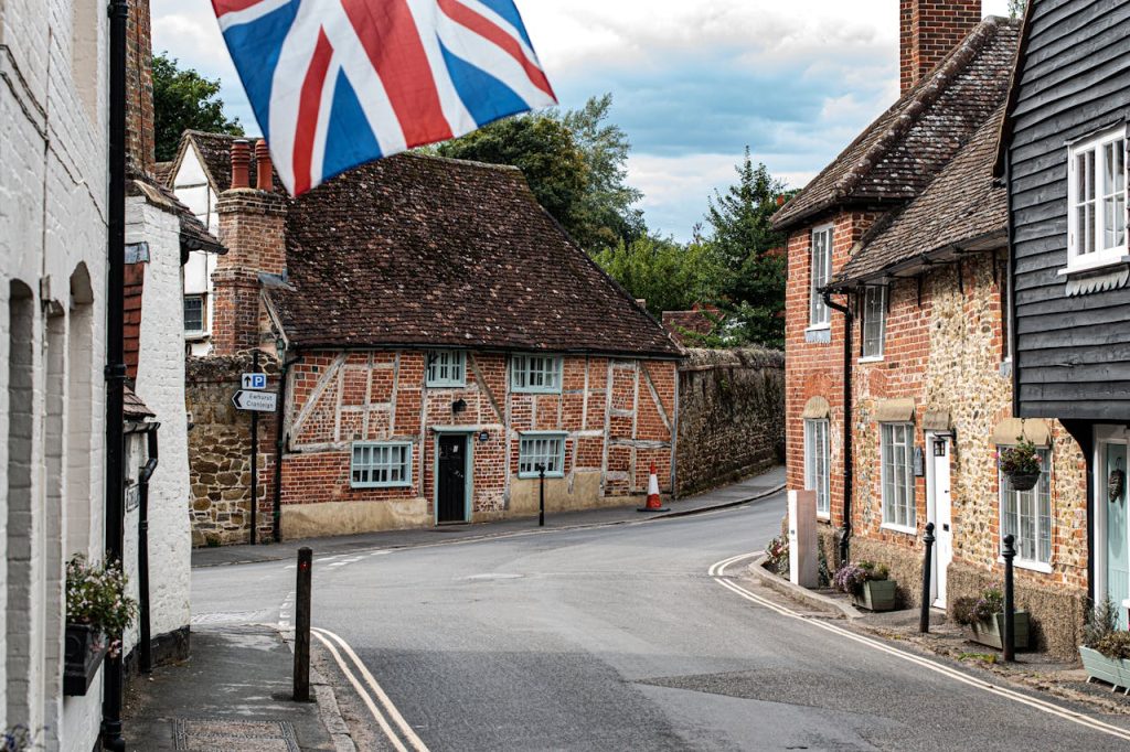 Scenic view of historic cottages in Shere, England, with a UK flag visible on a peaceful village street.