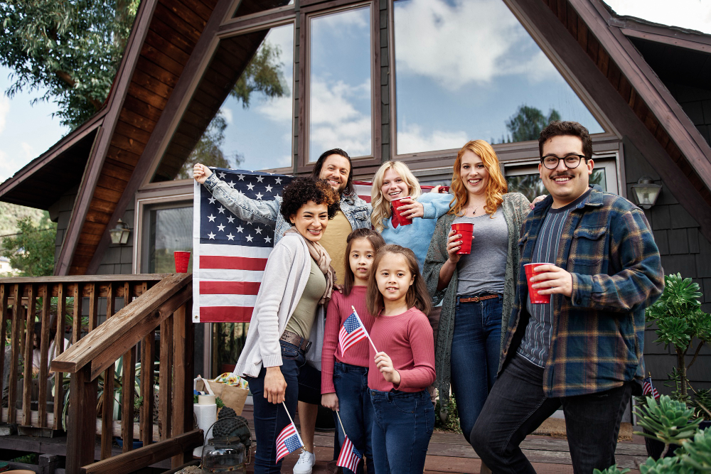 Outside their home, a family of four stands together, holding an American flag and celebrating their national pride